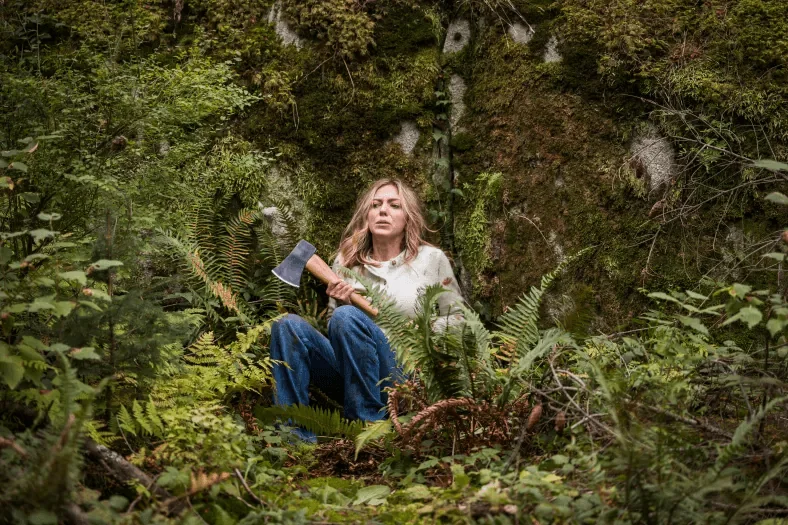 A woman sits among dense green ferns in a forest.